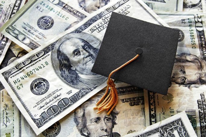 Graduation cap resting on a pile of US banknotes